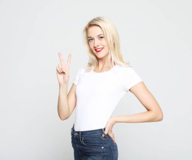 Sarı saçlı, beyaz tişörtlü genç bir kadın zafer işareti gösteriyor.