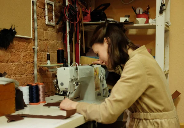 Ung kvinna arbetar i en verkstad, syr läderväskor — Stockfoto