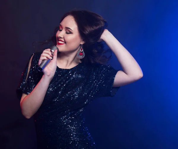 Estilo de vida y concepto de fiesta: Mujer joven en vestido negro con micrófono. — Foto de Stock