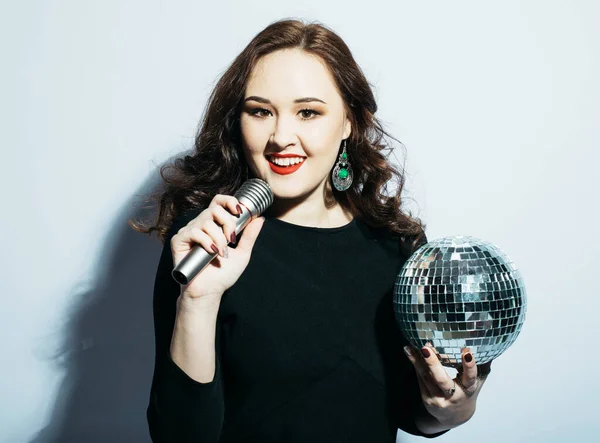 Beautiful woman holding a microphone and disco balls over white background. — Stock Photo, Image