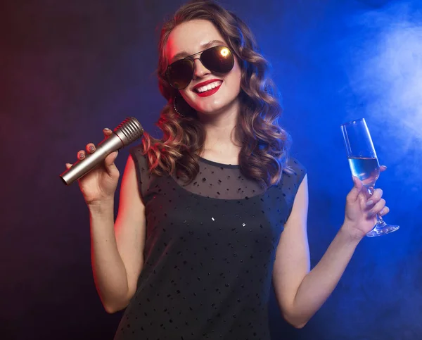 Genç mutlu kadın partide mikrofona şarkı söylüyor, mavi arkaplanda fotoğraf var.. — Stok fotoğraf