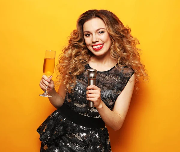 Feiern, Emotionen und Menschen. Glücklich lachende Frau trinkt Champagner und singt Weihnachtslied vor gelbem Hintergrund. — Stockfoto