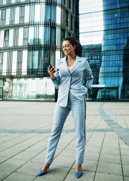 Mujer africana vestida con estilo de negocios en el fondo de un centro de negocios es la celebración de un teléfono móvil —  Fotos de Stock