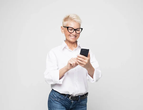 Ganska senior kvinna i casual outfit med modern smartphone — Stockfoto