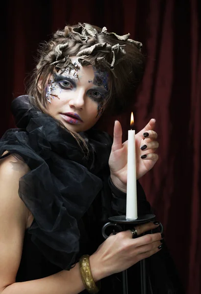 Joven hermosa mujer en un disfraz de bruja con maquillaje brillante y peinado está sosteniendo una vela. Halloween. Fiesta. Vacaciones. Carnaval.. —  Fotos de Stock