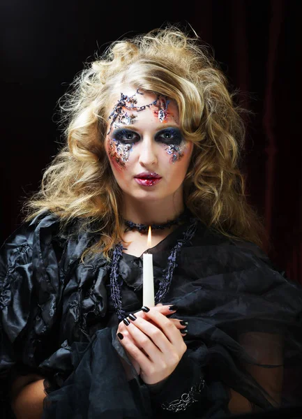 Joven hermosa mujer en un disfraz de bruja con maquillaje brillante y peinado está sosteniendo una vela. Halloween. Fiesta. Vacaciones. Carnaval.. — Foto de Stock