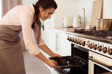 Genç kadın pasta şefi kek pişirmek için fırına koyar..