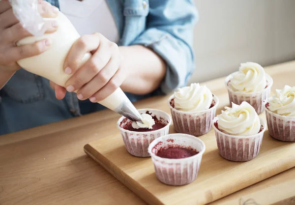 Estilo de vida, comida, gente y concepto de pequeña empresa: Una mujer joven decora magdalenas con crema blanca y bayas. —  Fotos de Stock