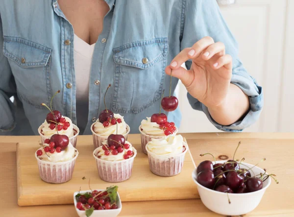 Stile di vita, cibo, persone e concetto di piccola impresa: una giovane donna decora muffin con panna bianca e bacche. — Foto Stock