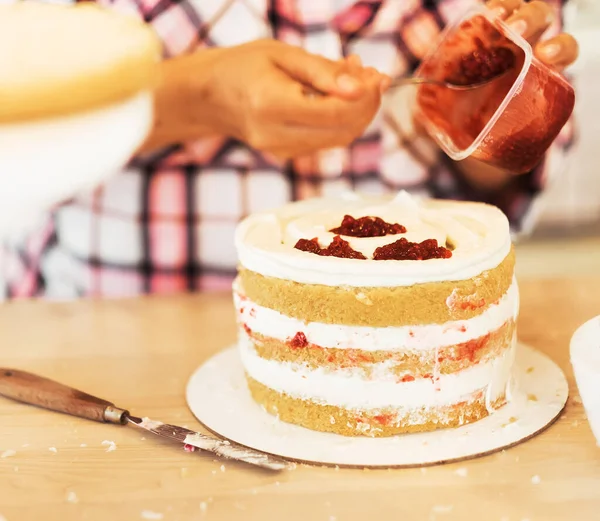 Молодая женщина-кондитер в фартуке смазывает торт вареньем. Вкусная выпечка. Хобби. Малый домашний бизнес. — стоковое фото