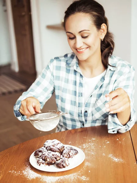Young woman pastry chef sprinkles icing sugar on chocolate chip cookies. Delicious pastries. Hobby. Small home business. — Stock Photo, Image