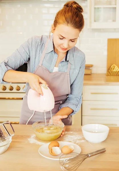 A young woman pastry chef in an apron beats eggs for the dough, for the future cake. Delicious pastries. — Stock Photo, Image