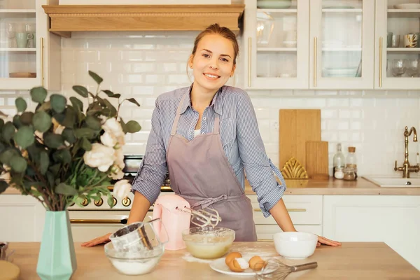 A young woman pastry chef in an apron beats eggs for the dough, for the future cake. Delicious pastries. — Stock Photo, Image
