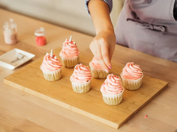 Una giovane donna decora i muffin con crema bianca nella sua cucina. — Foto Stock