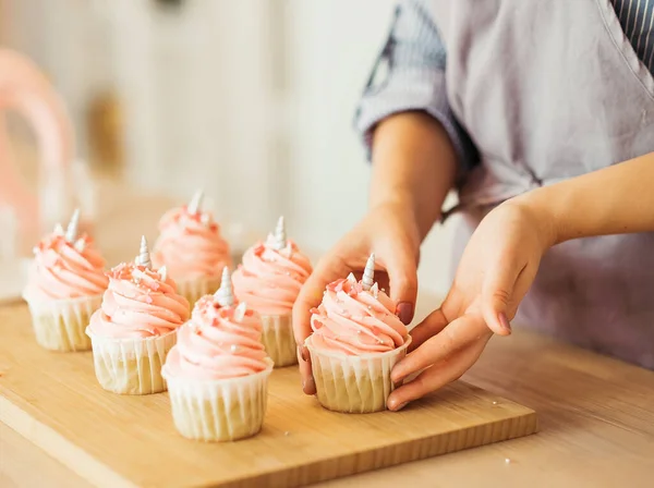 Una giovane donna decora i muffin con crema bianca nella sua cucina. — Foto Stock