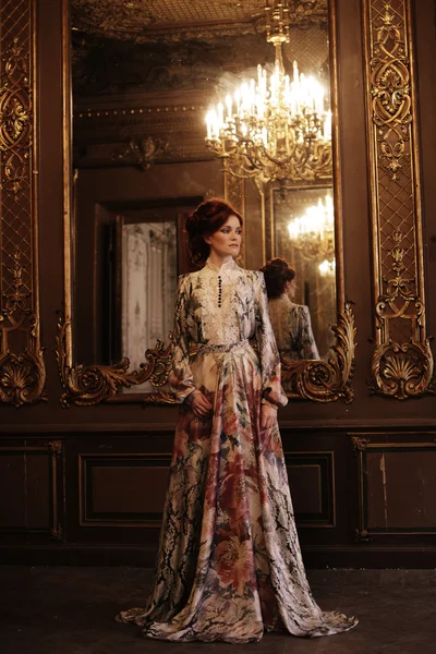 Vrouw staan in het paleis kamer met spiegel. — Stockfoto