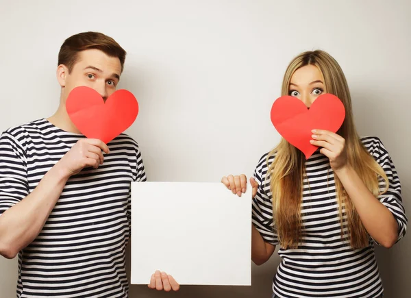 Feliz casal segurando branco em branco e corações vermelhos . — Fotografia de Stock