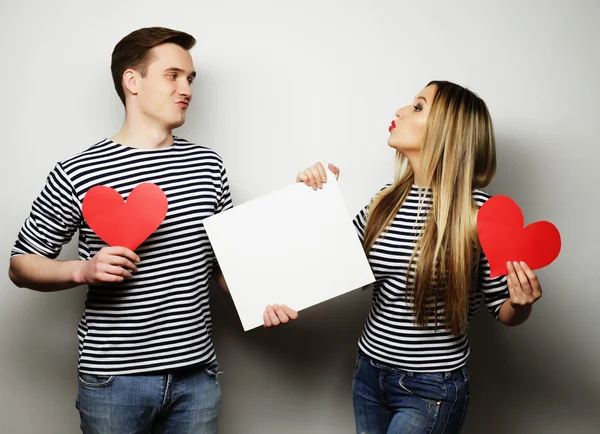 Feliz casal segurando branco em branco e corações vermelhos . — Fotografia de Stock