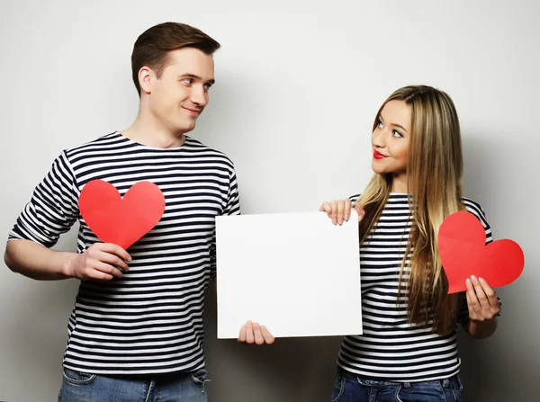 Happy couple holding white blank and red hearts. — Stock Photo, Image