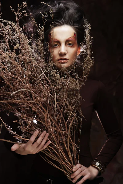 Kuru dallarla süslenmiş parlak bir kadın.