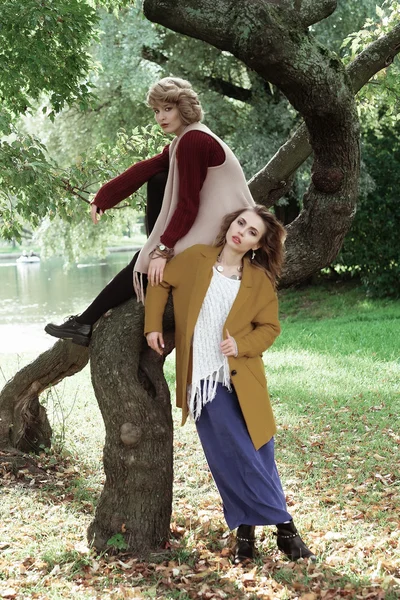 Δύο όμορφες νεαρές γυναίκες που θέτουν σε ένα δέντρο. — Φωτογραφία Αρχείου