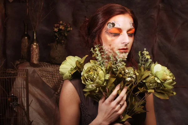 Жінка з яскравим креативним макіяжем тримає зелені квіти — стокове фото