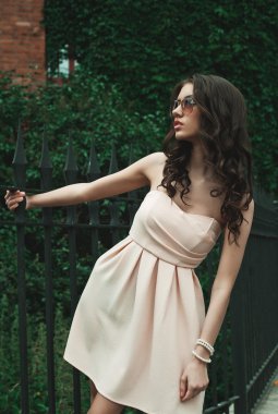 Güzel esmer, genç bir kadın elbise giyiyor ve sokakta yürüyor.