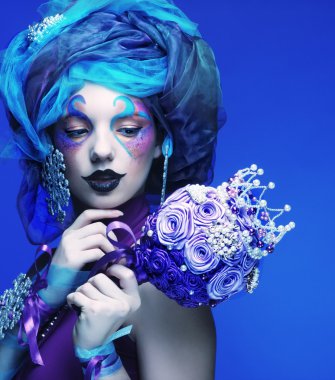 Yaratıcı makyajlı bir kadın bir buket mücevher tutuyor.