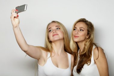 İki genç kadın cep telefonuyla selfie çekiyor.