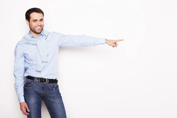 Joven hombre sonriente señala con los dedos en el lado derecho — Foto de Stock