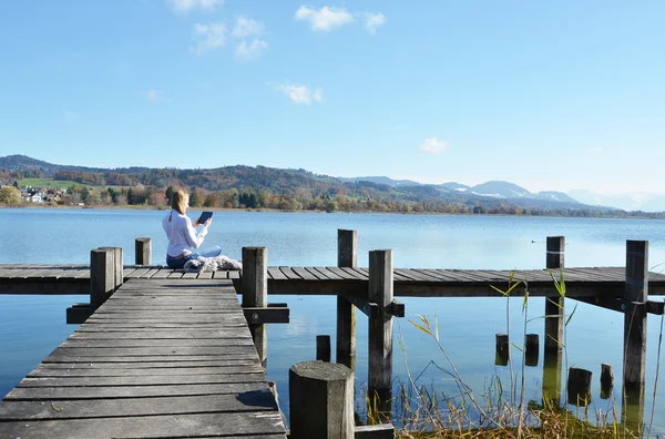 Meisje lezing Tablet PC tegen lake. — Stockfoto