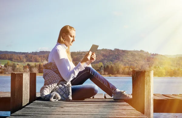 Meisje lezing Tablet PC tegen lake. — Stockfoto