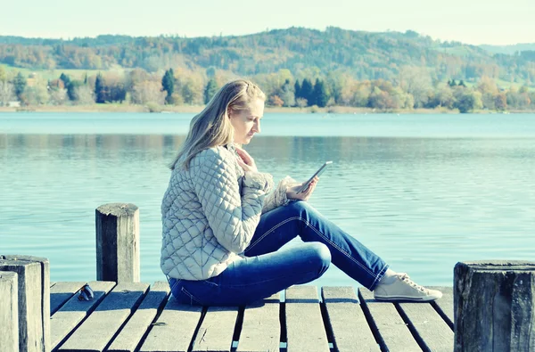 Dívka čtení tablet proti jezero. — Stock fotografie