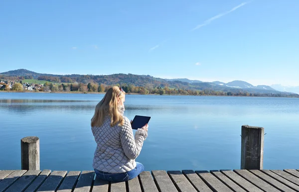 Girl reading  tablet  against  lake. — Stock Photo, Image