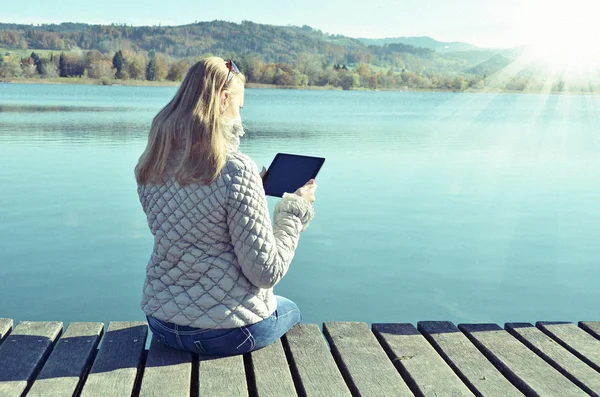 Mädchen liest Tablet gegen See. — Stockfoto