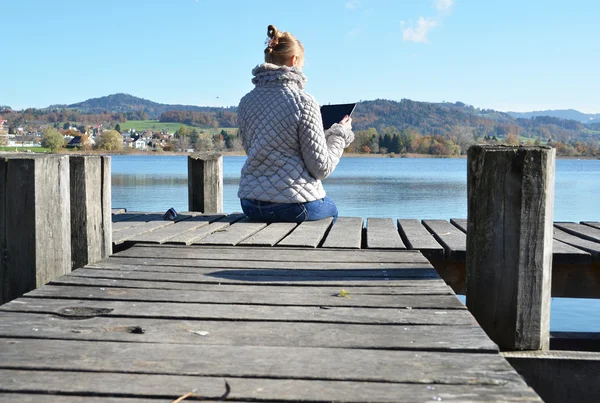 Girl reading from tablet near lake — Stock Photo, Image