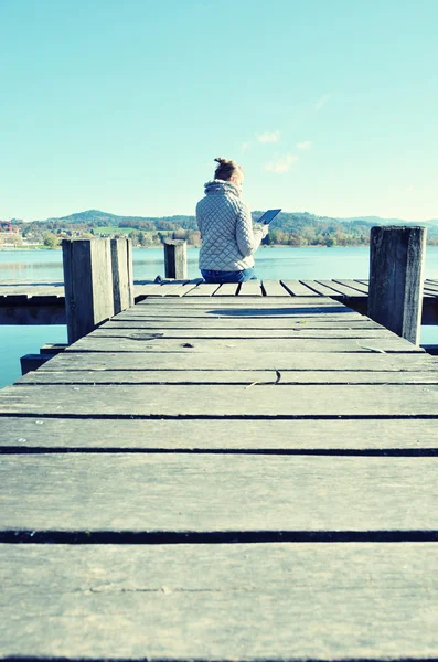 Chica leyendo desde la tableta cerca del lago . — Foto de Stock