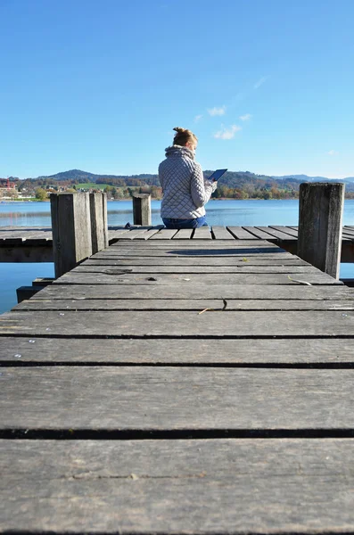 Girl reading from a tablet on jetty — Stock Photo, Image