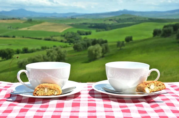 Kávé és toszkán cantuccinikávé és cantuccini a toszkán táj ellen fából készült asztal. Olaszország Stock Kép