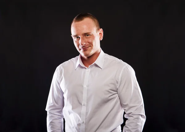 Young smiling man in white shirt over dark background — Stock Photo, Image