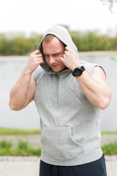 Workout-Mann in Kapuze ruht sich am Fluss aus. — Stockfoto