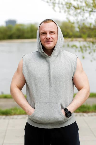 Workout-Mann in Kapuze ruht sich am Fluss aus. — Stockfoto