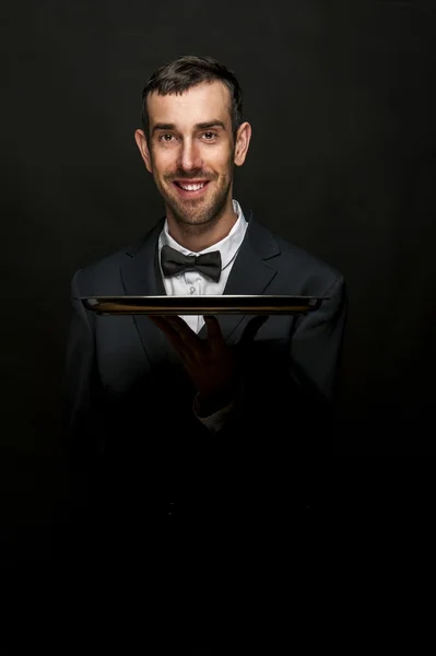 Waiter in black suit holding tray over black background. — Stock Photo, Image