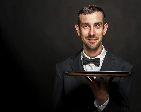 Waiter in black suit holding tray over black background. — Stock Photo, Image