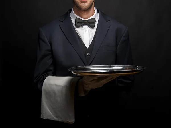 Waiter in black suit holding tray over black background. — Stock Photo, Image