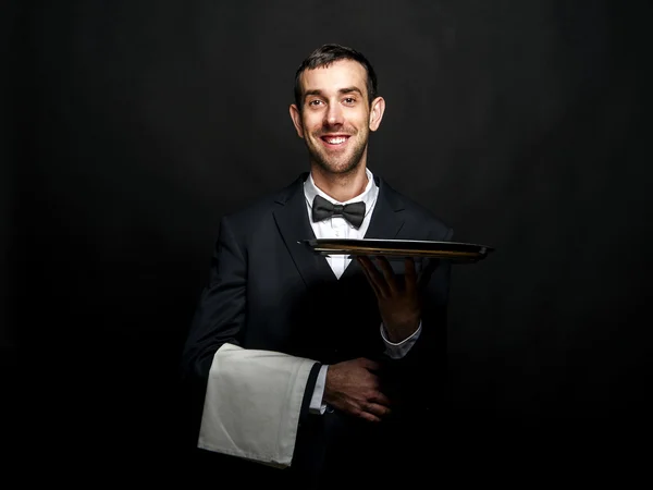 Číšník v černém obleku drží podnos na černém pozadí. — Stock fotografie