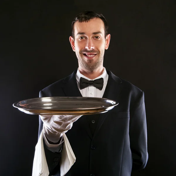 Waiter in black suit holding tray over black background. — Stock Photo, Image