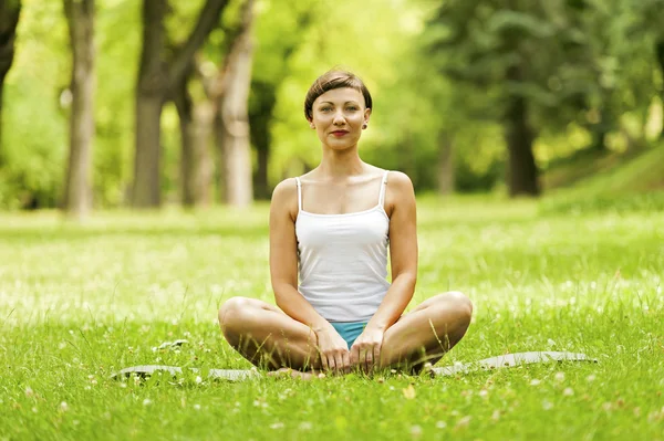 Siting yoga kadınla çimenlerin üzerinde dinlenmek ve gülümseyen. — Stok fotoğraf