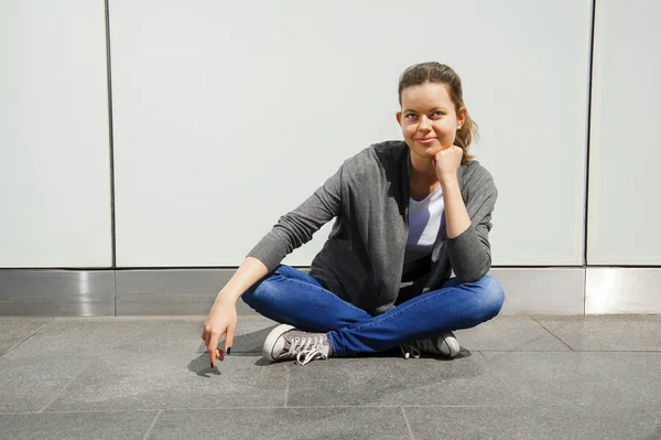 Mooie modieuze jonge vrouw zitten op straat door de muur met — Stockfoto