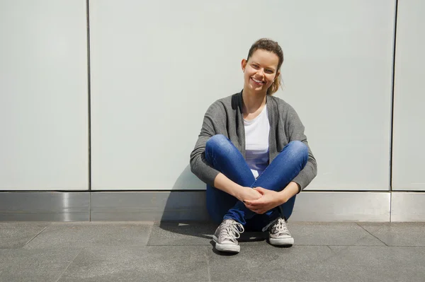 Belle jeune femme à la mode s'asseoir sur la rue au mur avec — Photo